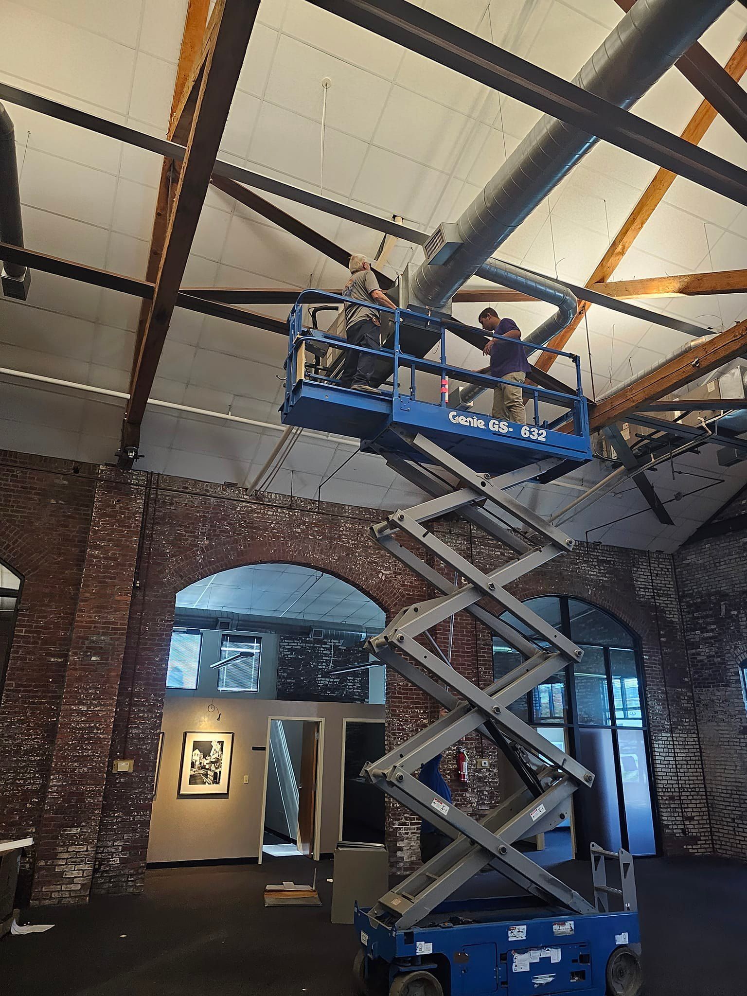 A man is standing on a scissor lift working on a ceiling.
