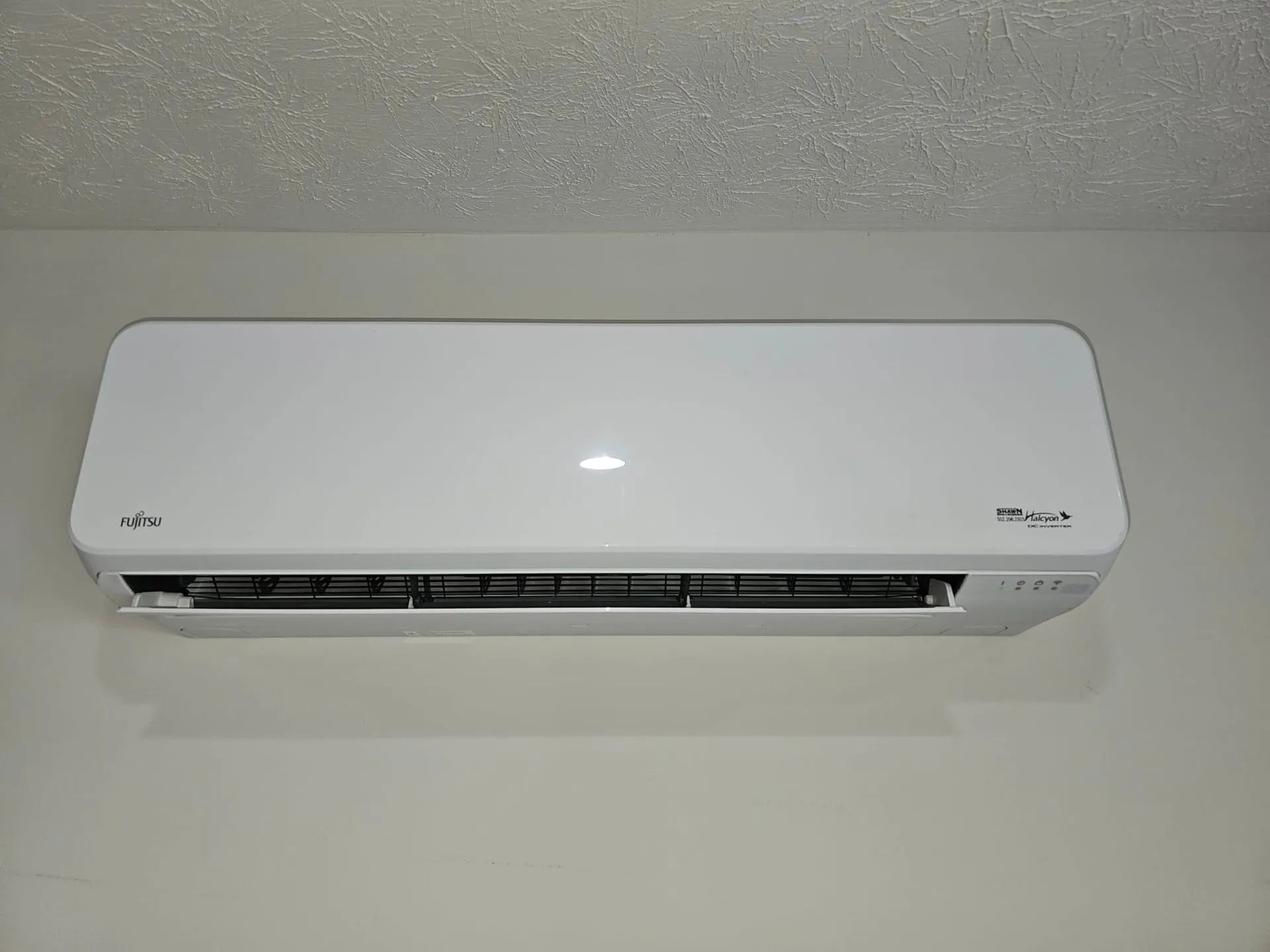 A white rectangular wall-mounted air conditioning unit centered against a white wall.