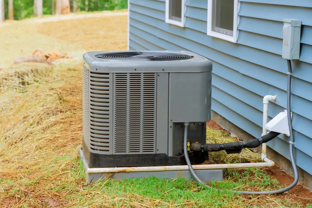 Air conditioning unit next to a blue-sided house with a grassy yard.
