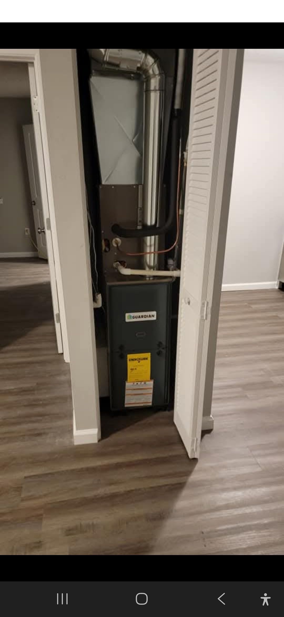 A furnace enclosed in a closet with open doors; interior with wood-like flooring and neutral walls.