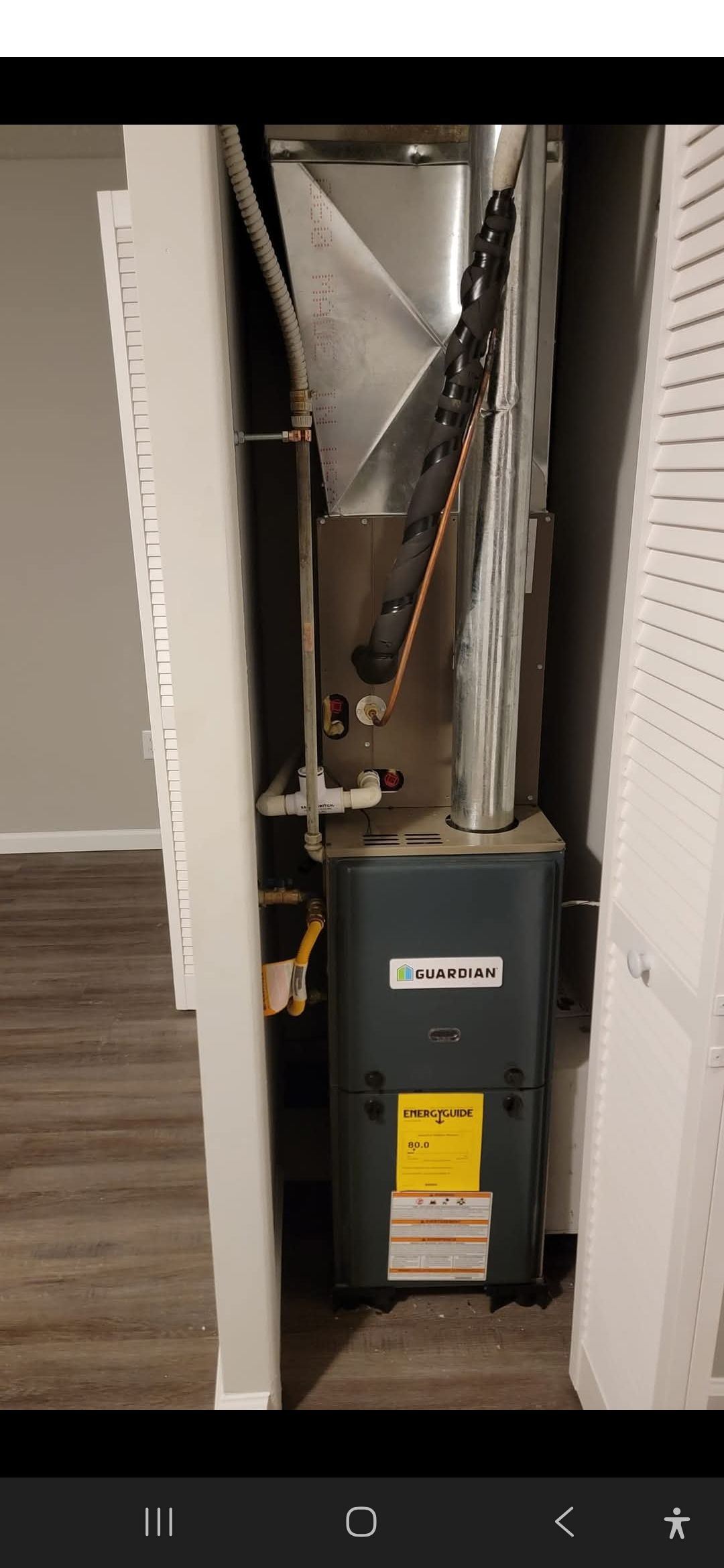 Furnace unit inside a closet with closed louvered doors. Includes yellow energy efficiency sticker on the front.