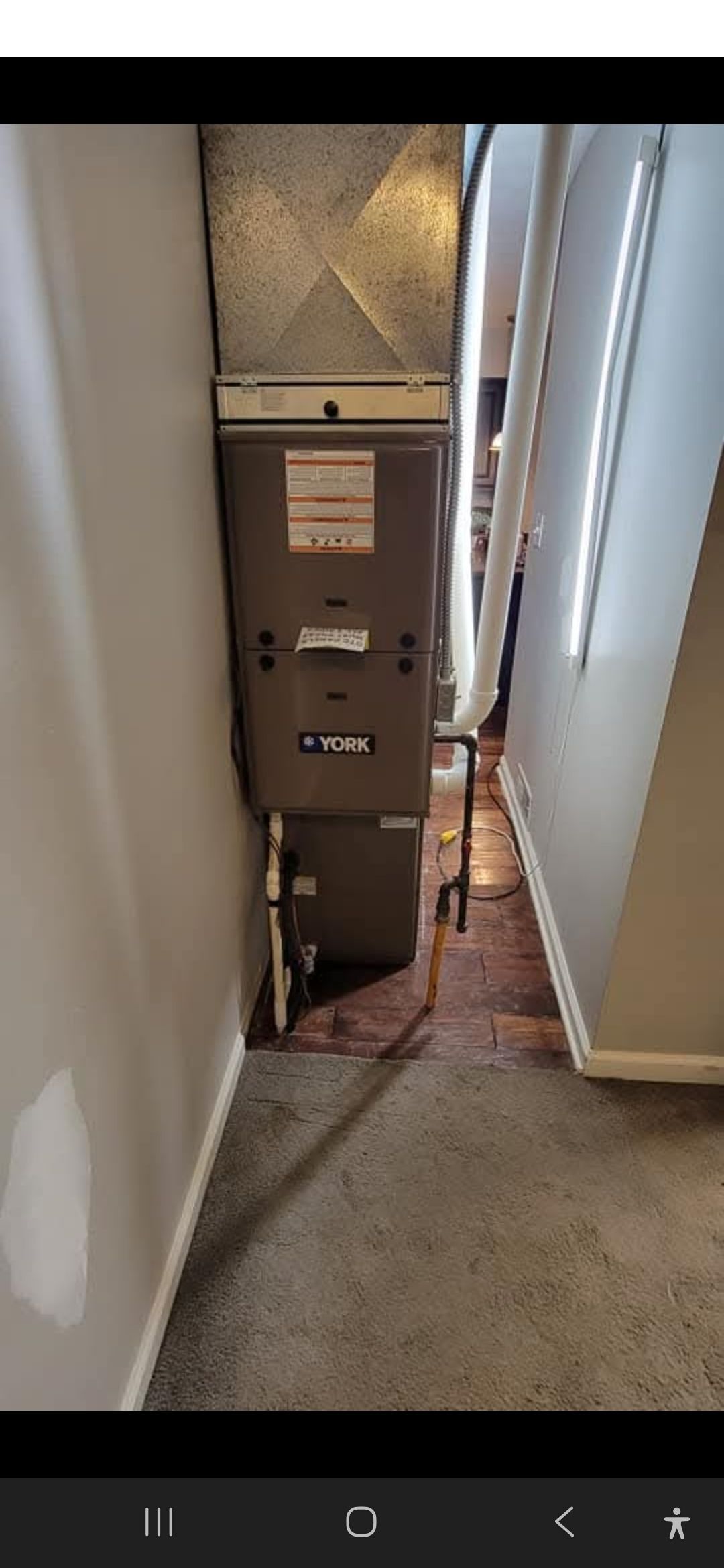 Furnace unit in a narrow hallway with carpet and hardwood floors.