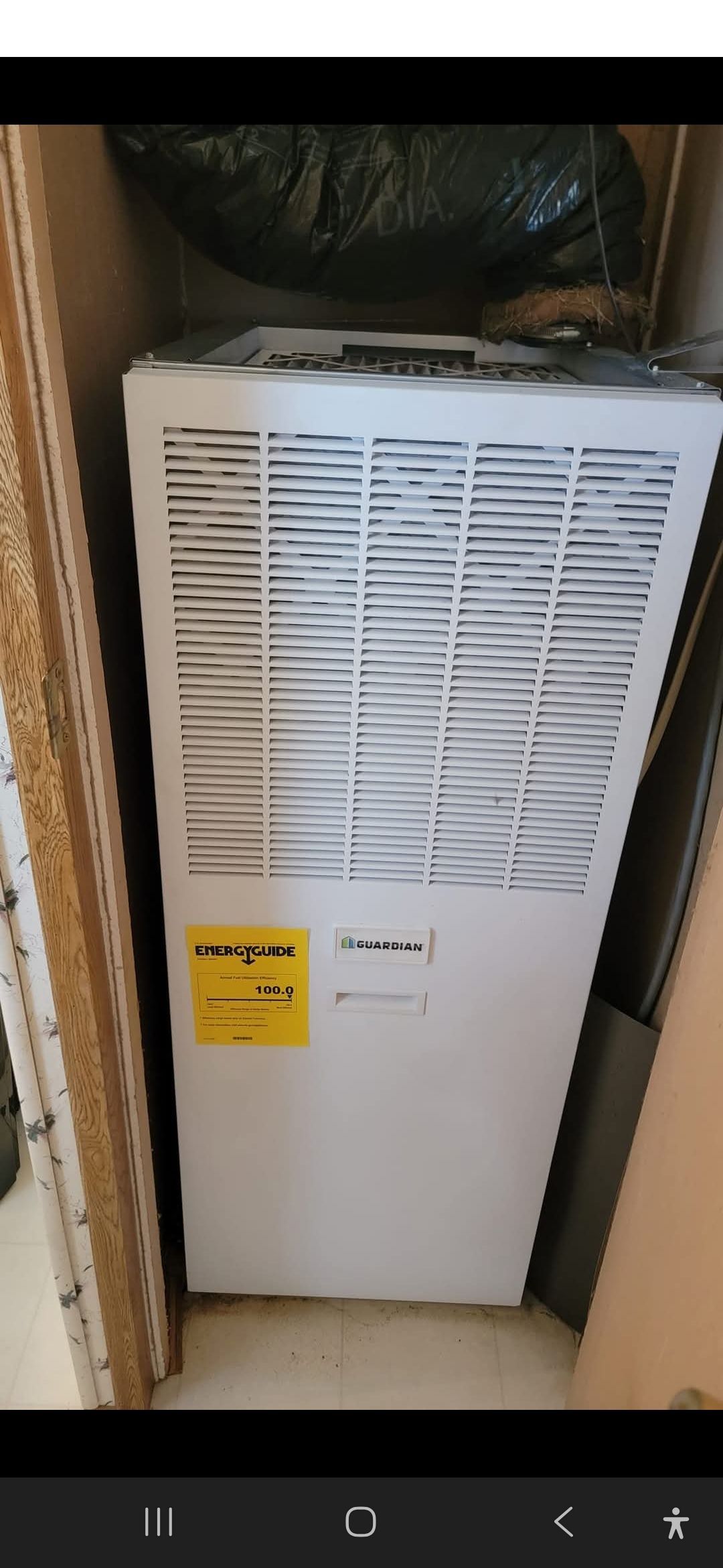 White air handler unit with a yellow energy guide label. It is in a closet.