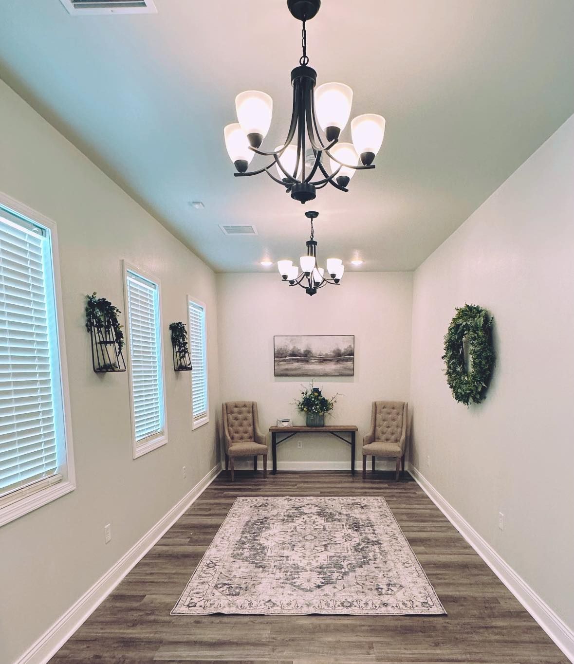 Bright hallway with chandeliers, bench, chairs, wall decor, windows, and a patterned rug.