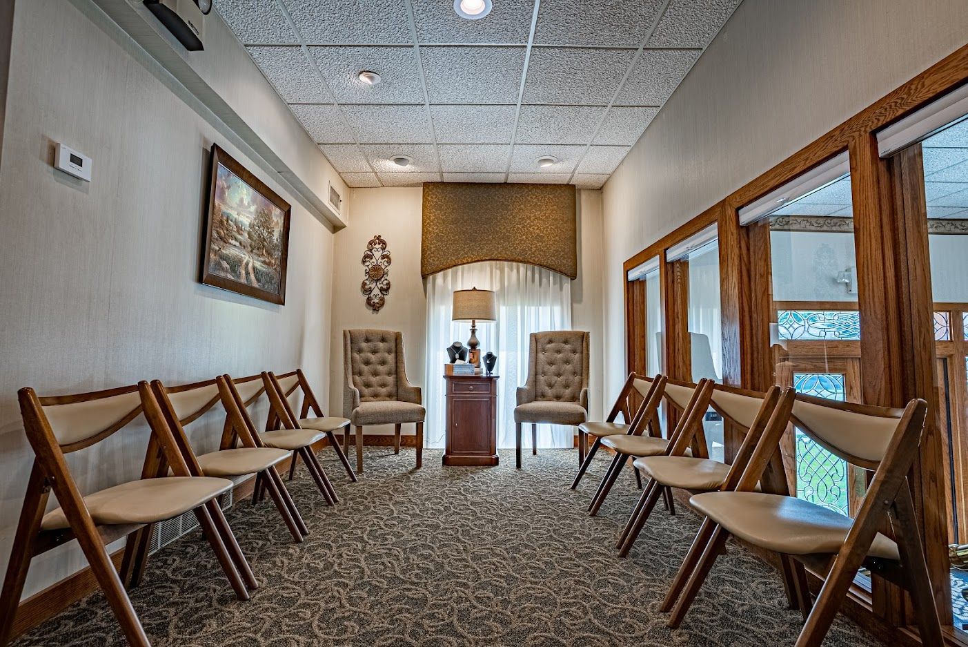 Empty waiting room with rows of tan chairs, patterned carpet, and bright windows along one wall