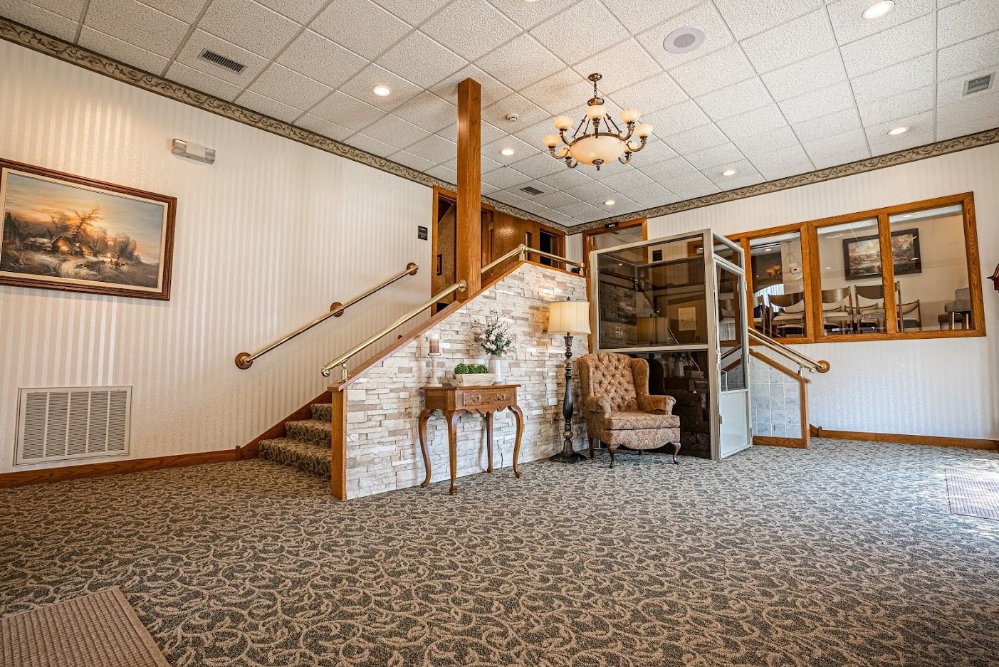 Empty carpeted lobby with stone staircase, chandelier, and wood-paneled reception area