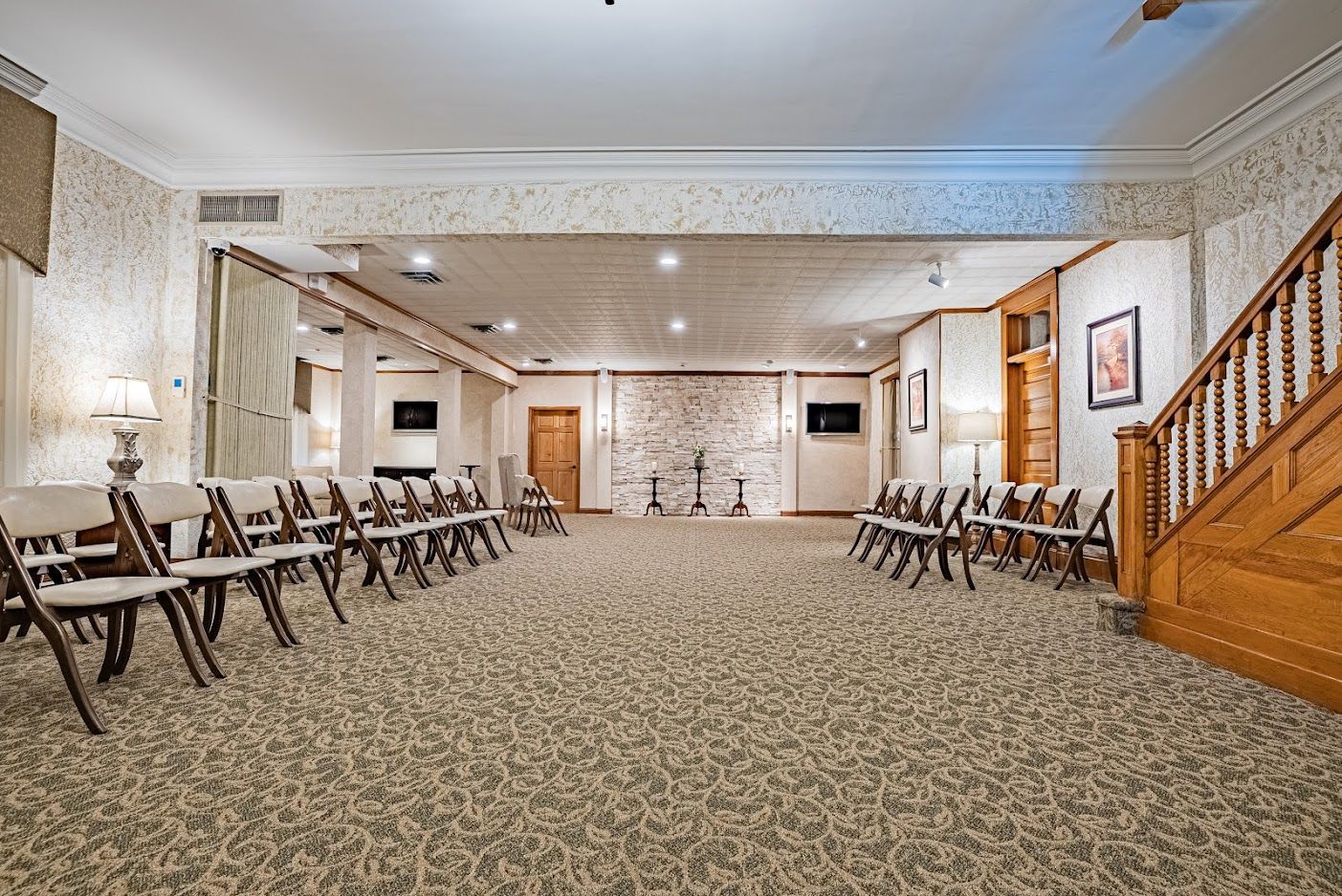 Empty banquet hall with rows of chairs, patterned carpet, and a wooden staircase on the right