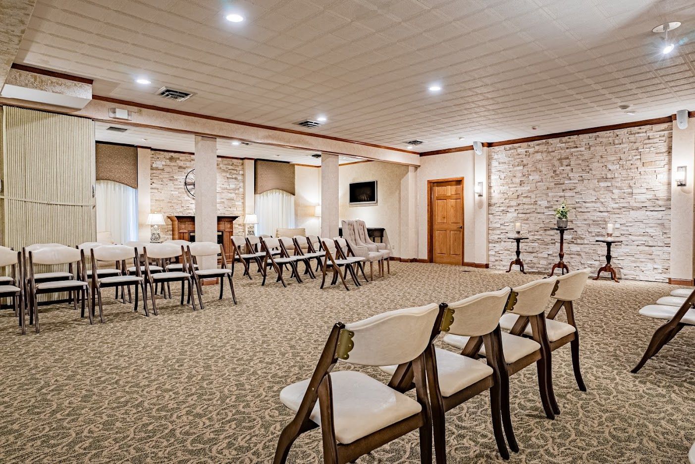 Empty banquet hall with rows of chairs, brick walls, and a tiled floor lit by recessed ceiling lights