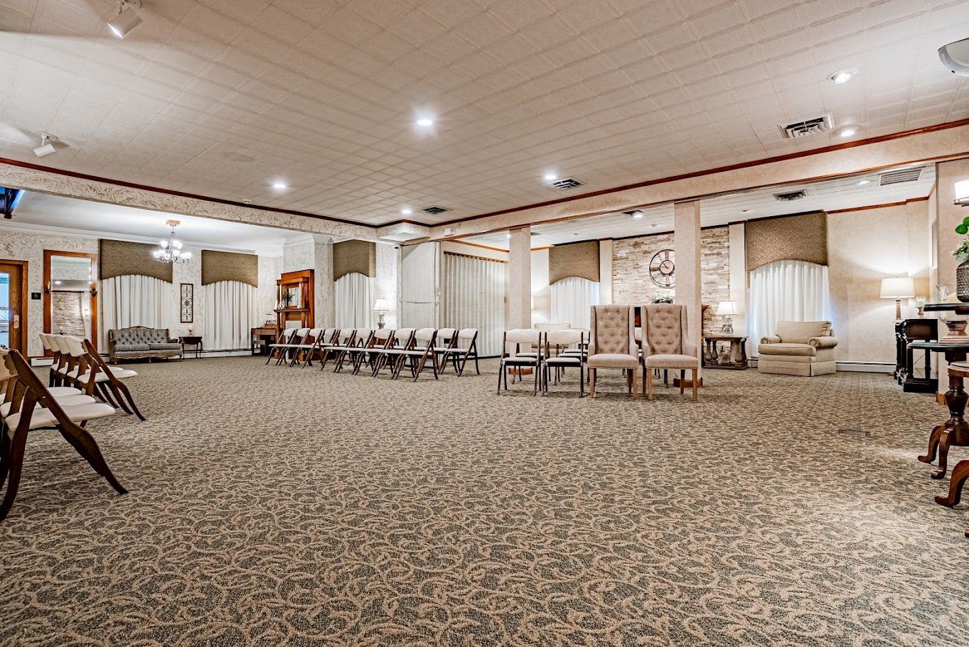 Spacious banquet hall with carpeted floor, round tables, chairs, and bright recessed lighting.