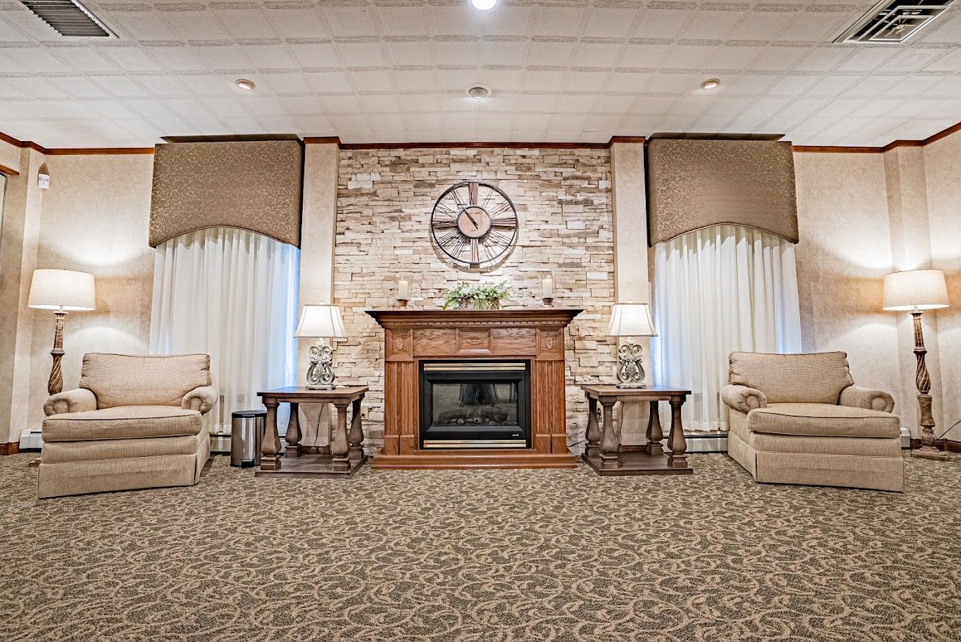 Cozy lounge with fireplace, stone wall, clock, and matching armchairs on a patterned carpet