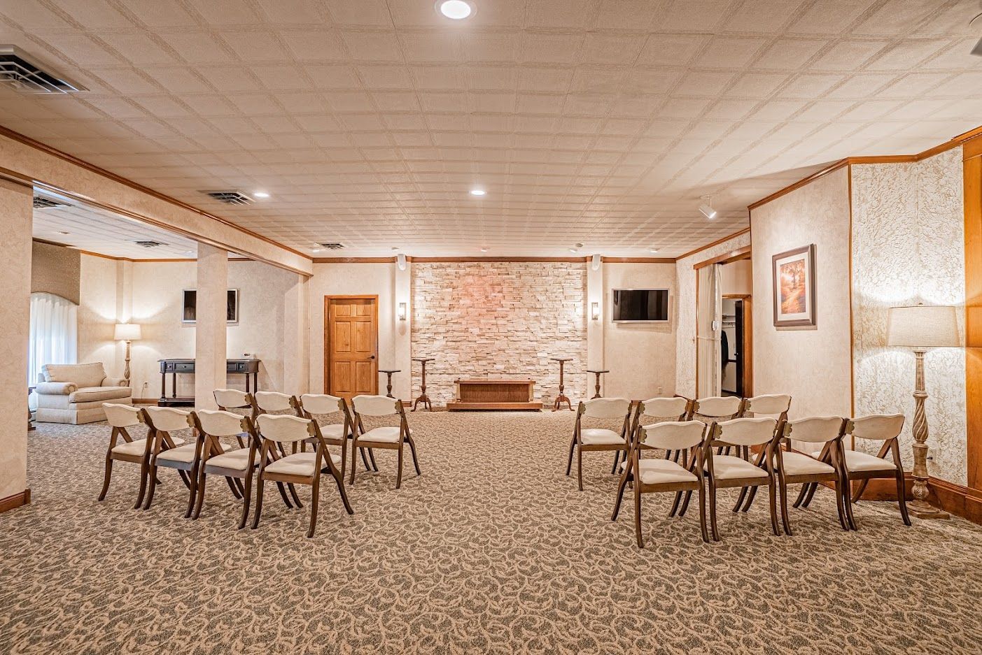 Spacious meeting room with rows of chairs, carpeted floor, and a brick accent wall at the front