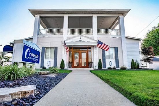 White two-story office building with columns, American flags, lawn, and a sign by the entrance