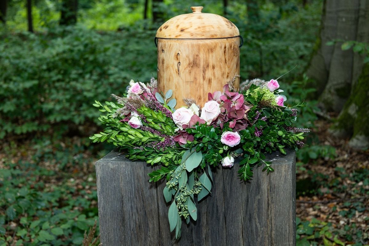 Floral arrangement with pink and purple flowers around a wooden stump in a forest setting