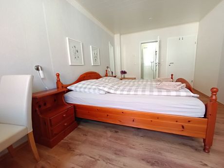Schlafzimmer mit Holzbett, Nachttisch und weißem Stuhl.