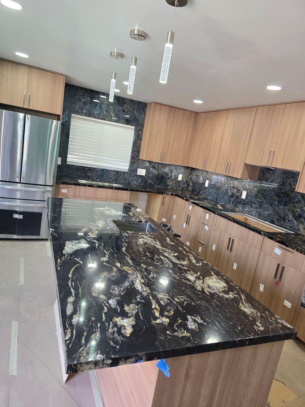Modern kitchen with black marble island, wood cabinets, stainless appliances, and pendant lights