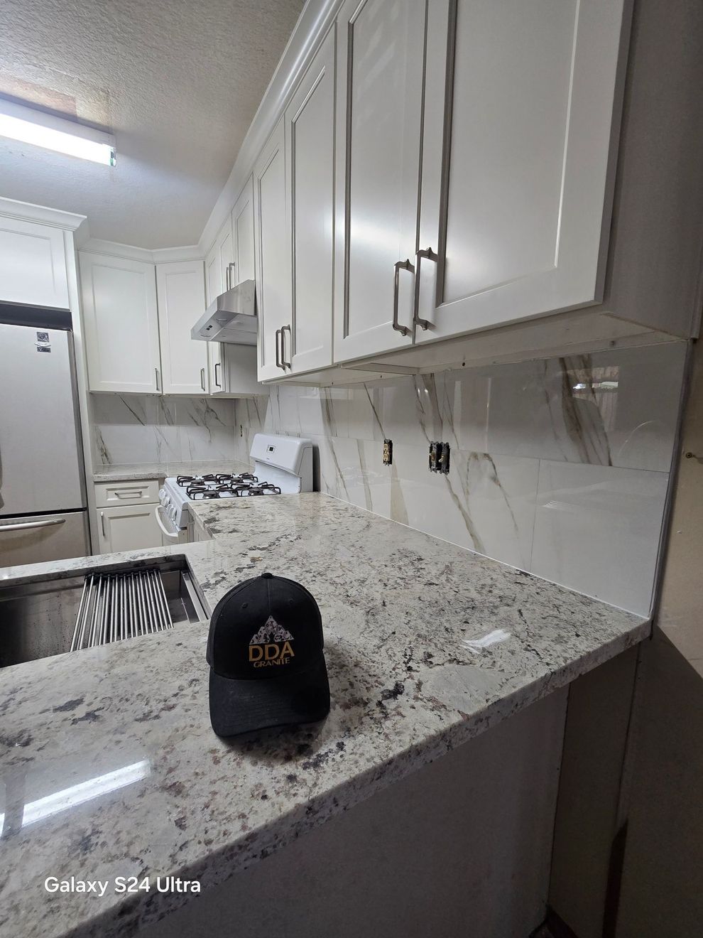 Bright white kitchen with granite counters, cabinets, and a black cap on the island.