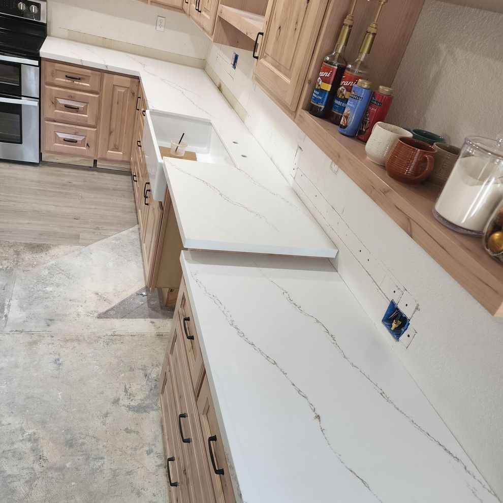 Kitchen under renovation with white countertops, unfinished cabinets, and tools on a shelf.