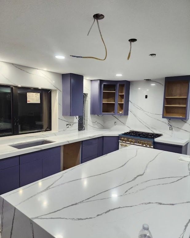 Modern kitchen with white marble island, purple cabinets, and unfinished ceiling lights.