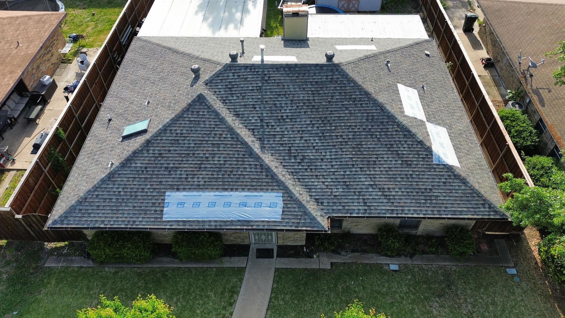 Aerial view of a house with a dark grey roof, surrounded by a wooden fence, and a green lawn.