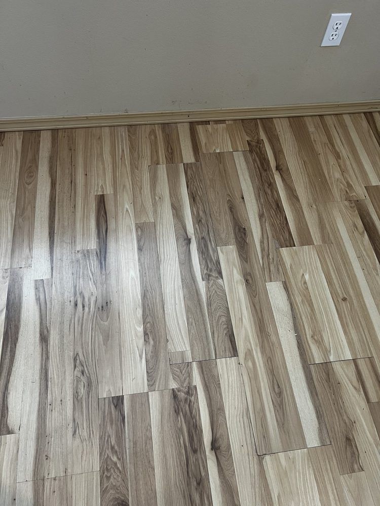 Wood-look laminate floor meeting a beige wall with a white electrical outlet.