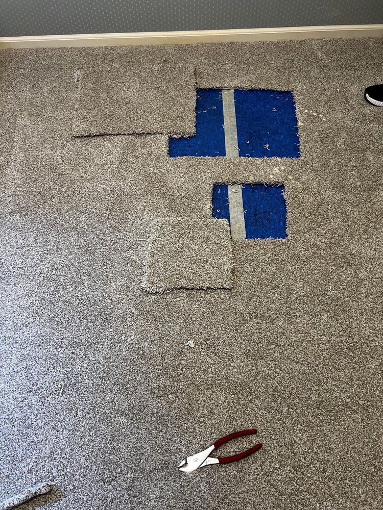 Carpeted floor with blue tape markings, a small white paper scrap, and red-handled pliers.