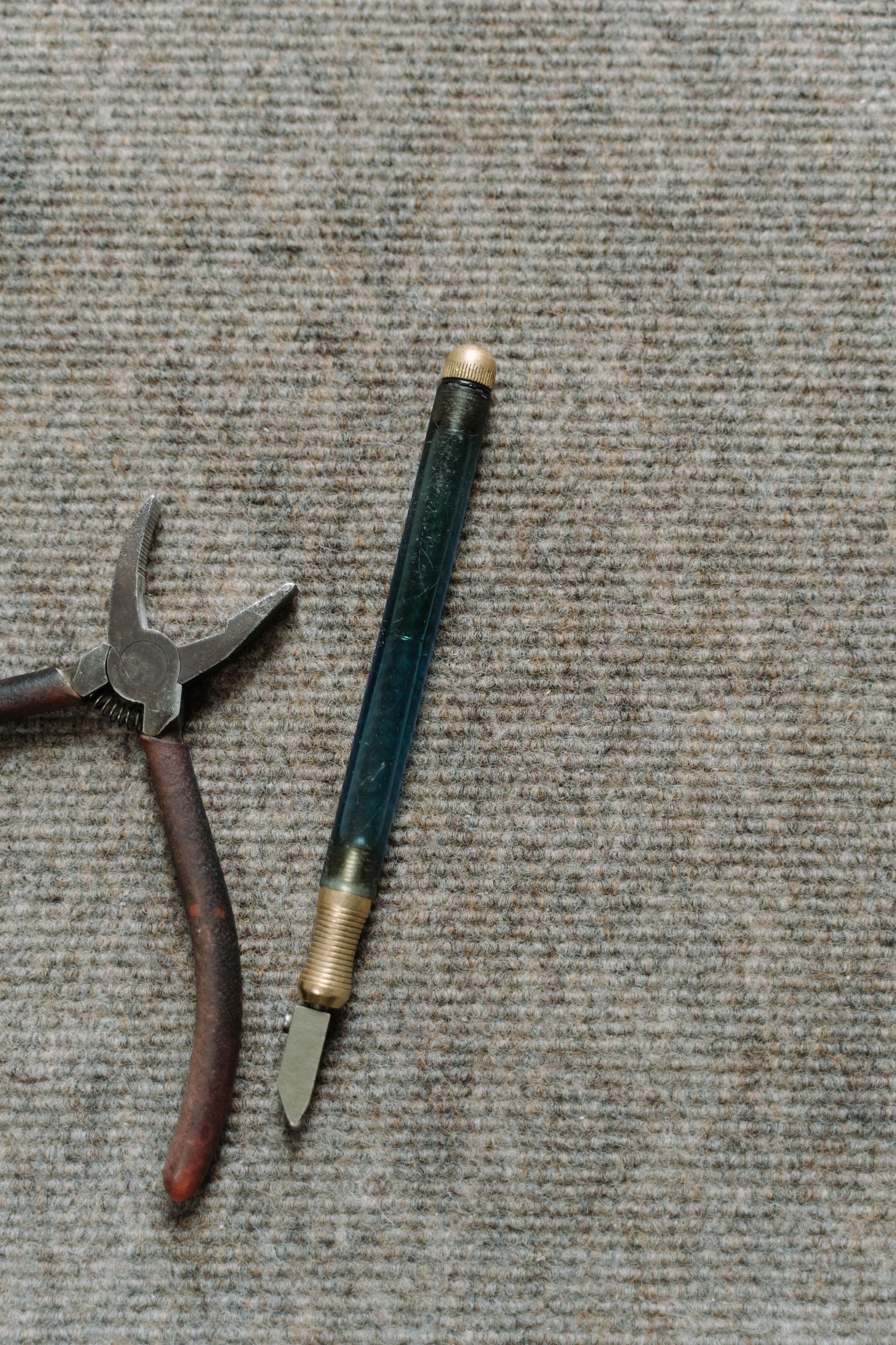 Needle-nose pliers and a blue-handled craft knife on a gray fabric surface.