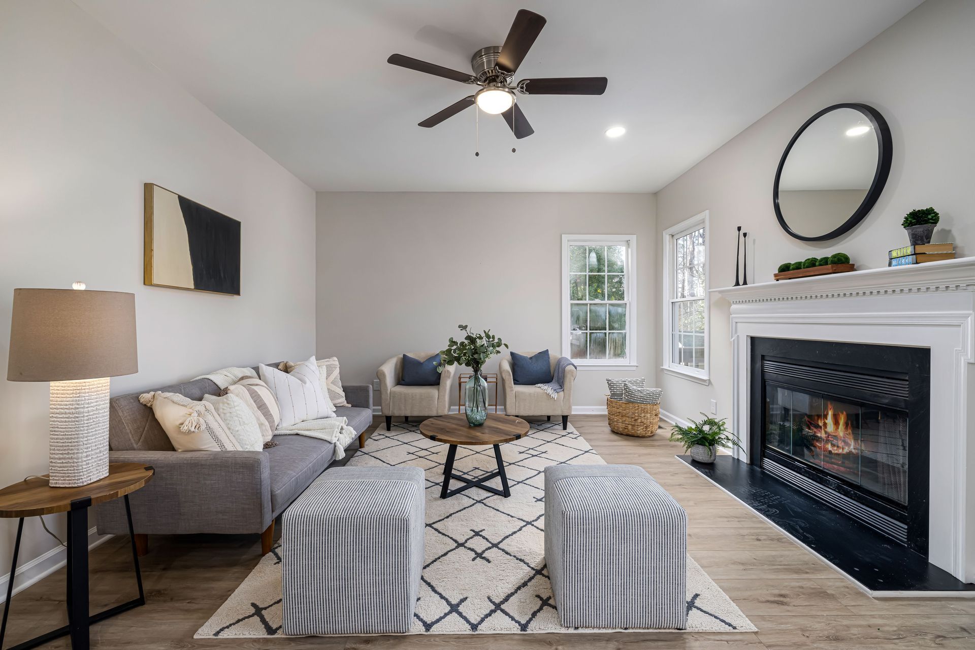 Bright living room with gray sofa, striped ottomans, fireplace, and ceiling fan