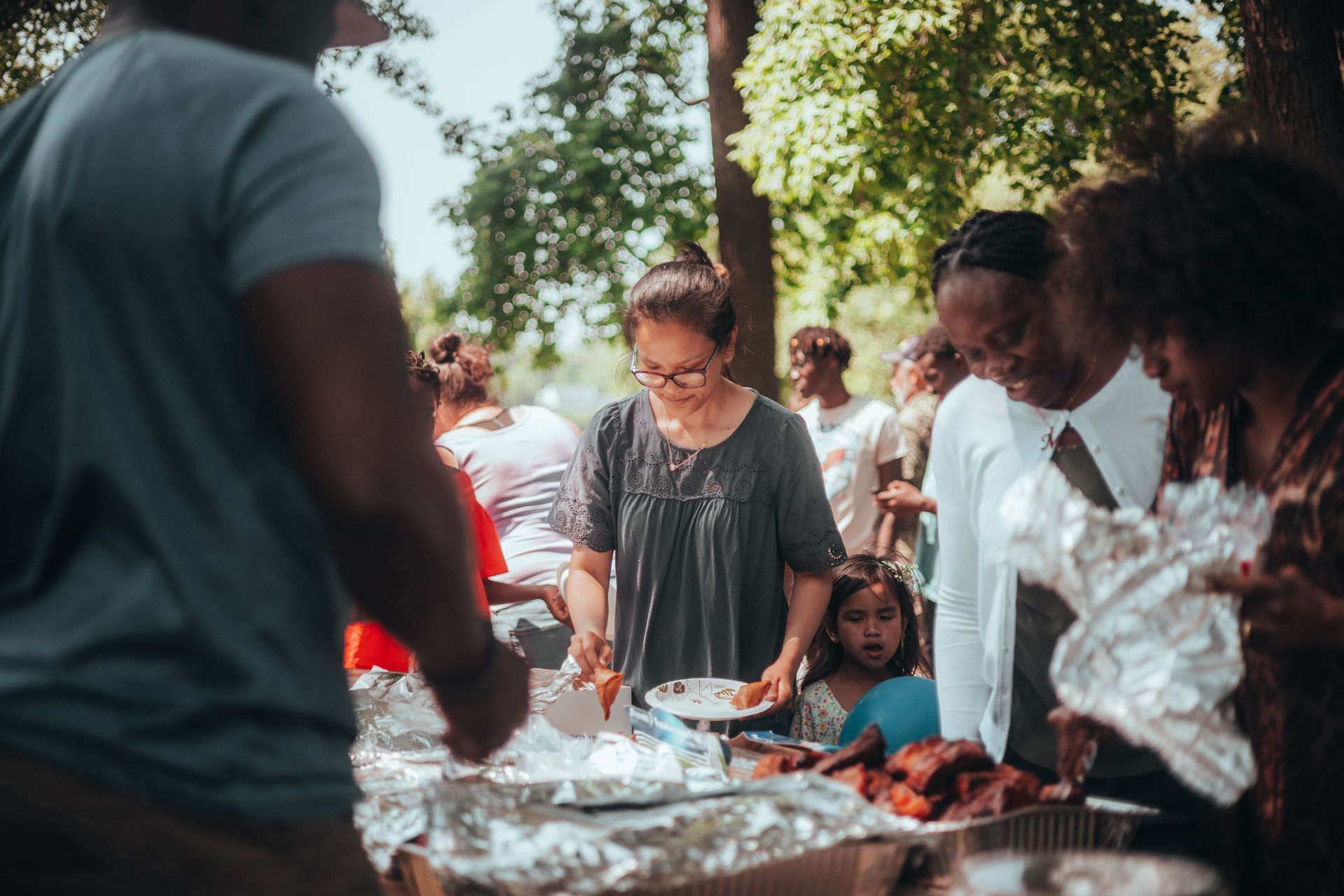 People serving food at an outdoor community gathering under trees