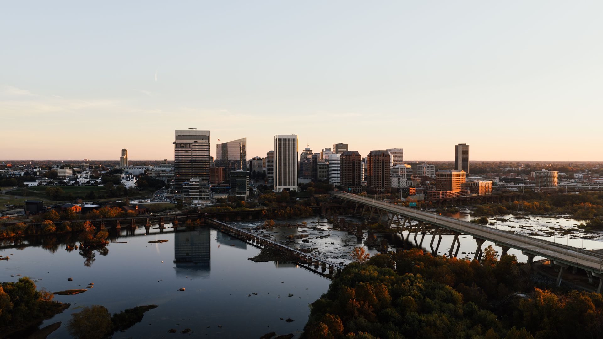 City skyline at sunset over a river with bridges and autumn trees in the foreground