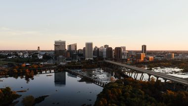 City skyline at sunset over a river with bridges and autumn trees in the foreground