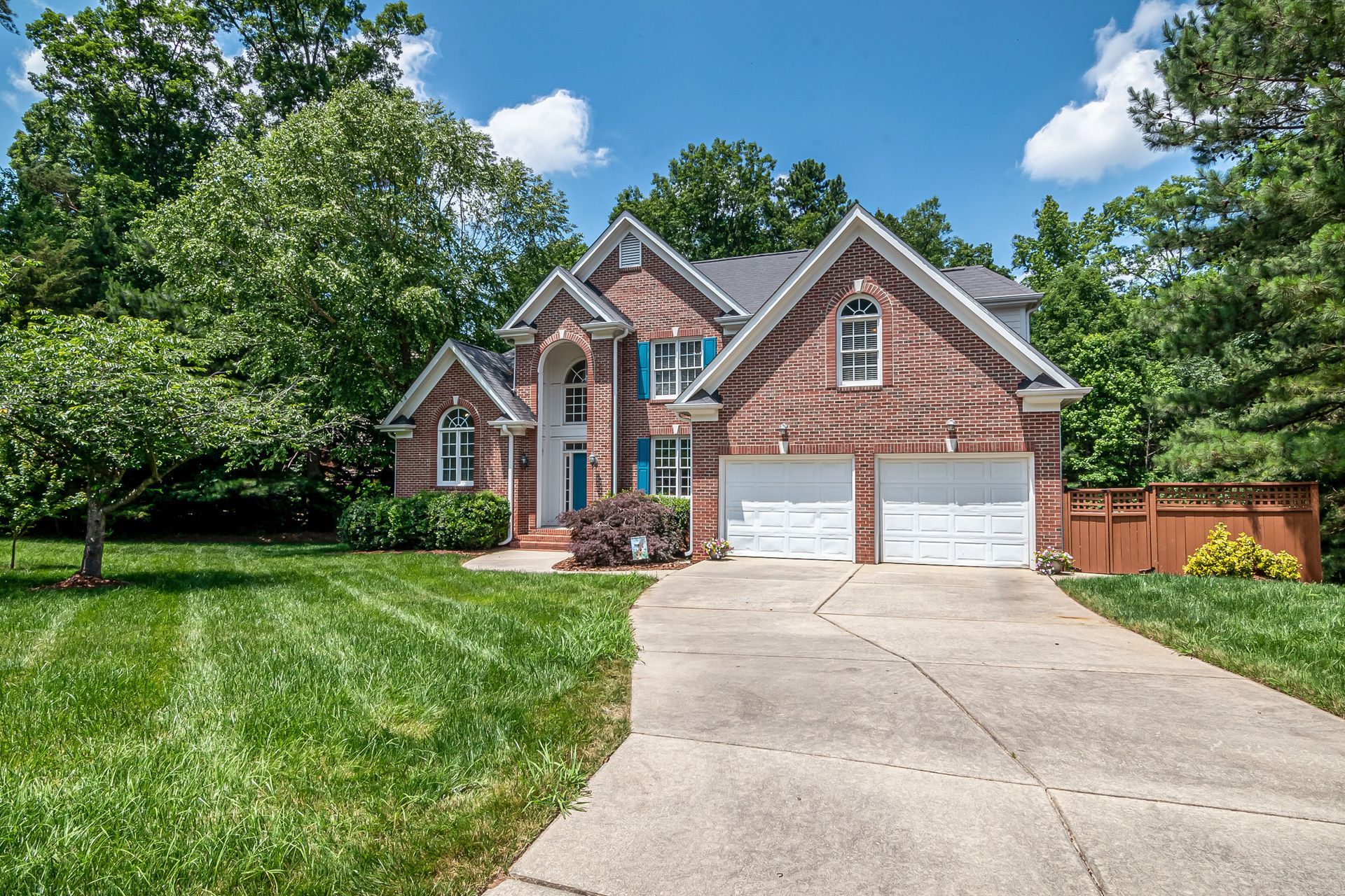 Brick suburban house with two-car garage, curved driveway, and green lawn under a blue sky