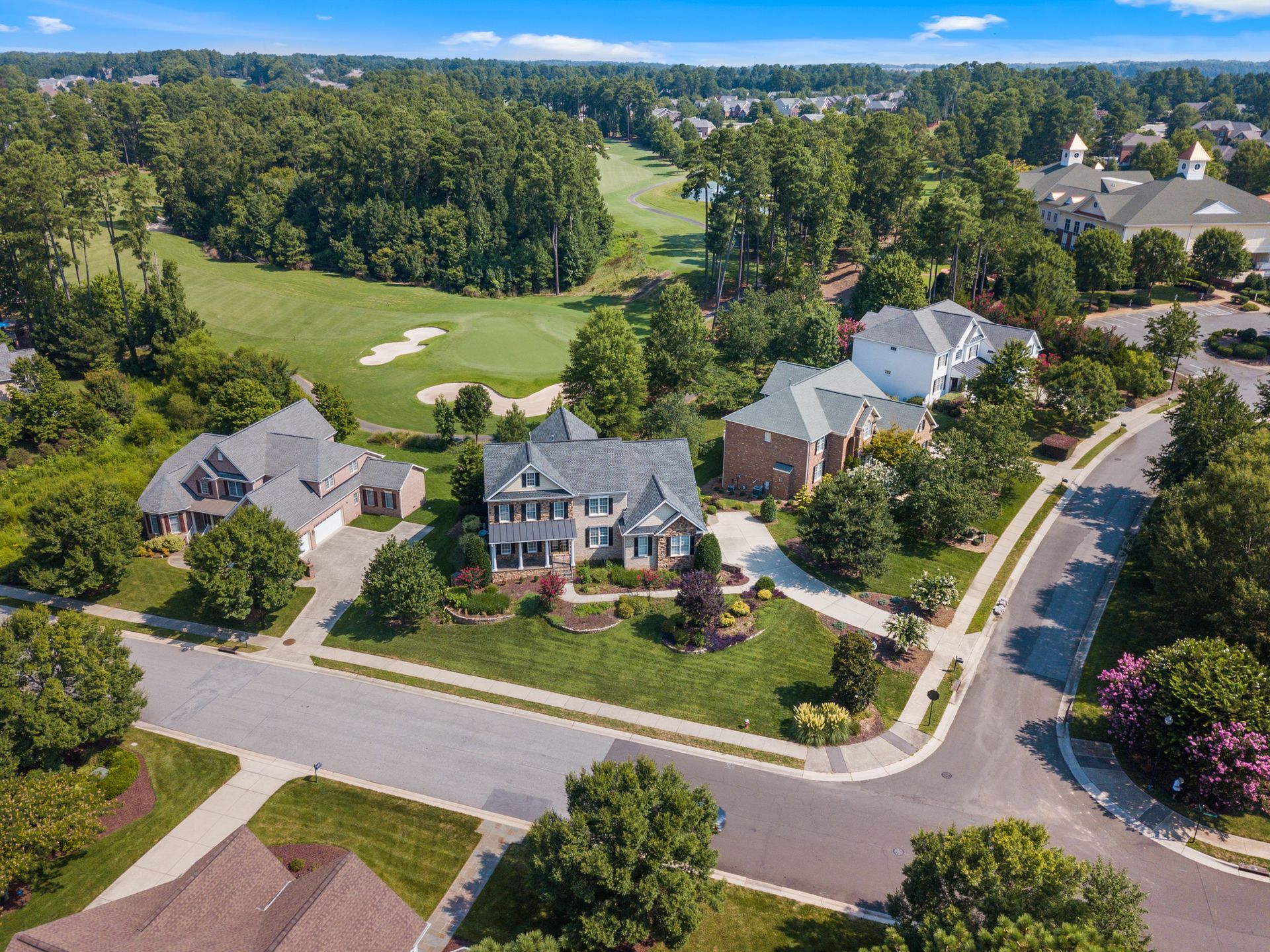 Aerial view of suburban homes beside a golf course and tree-lined roads.