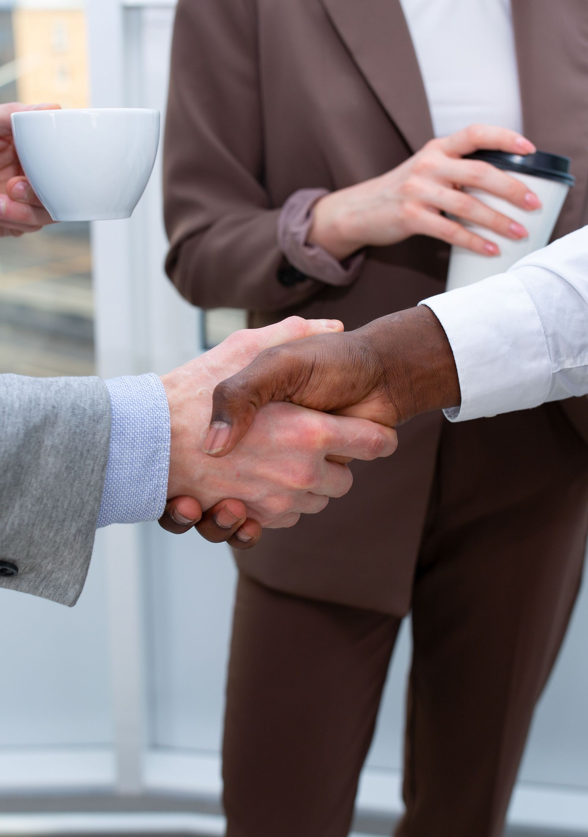 Handshake in an office, with people holding coffee cups and a takeaway cup nearby.