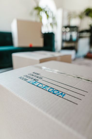 Stacked white cardboard boxes in a blurred office, with one box labeled “ROOM” in blue.