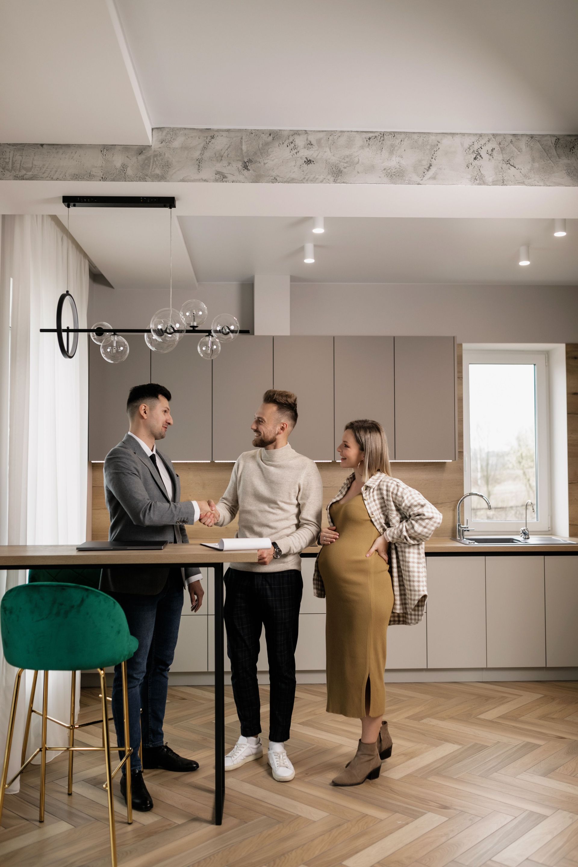 Three people chatting at a high table in a bright modern kitchen, with one holding a coffee cup.