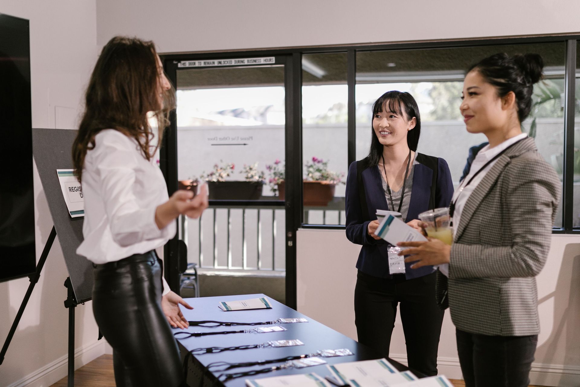 Three people talking by a table with brochures in a bright office or lobby.