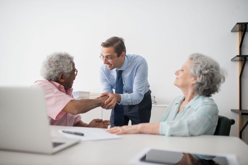 Healthcare worker greeting two elderly patients across a table in a bright office