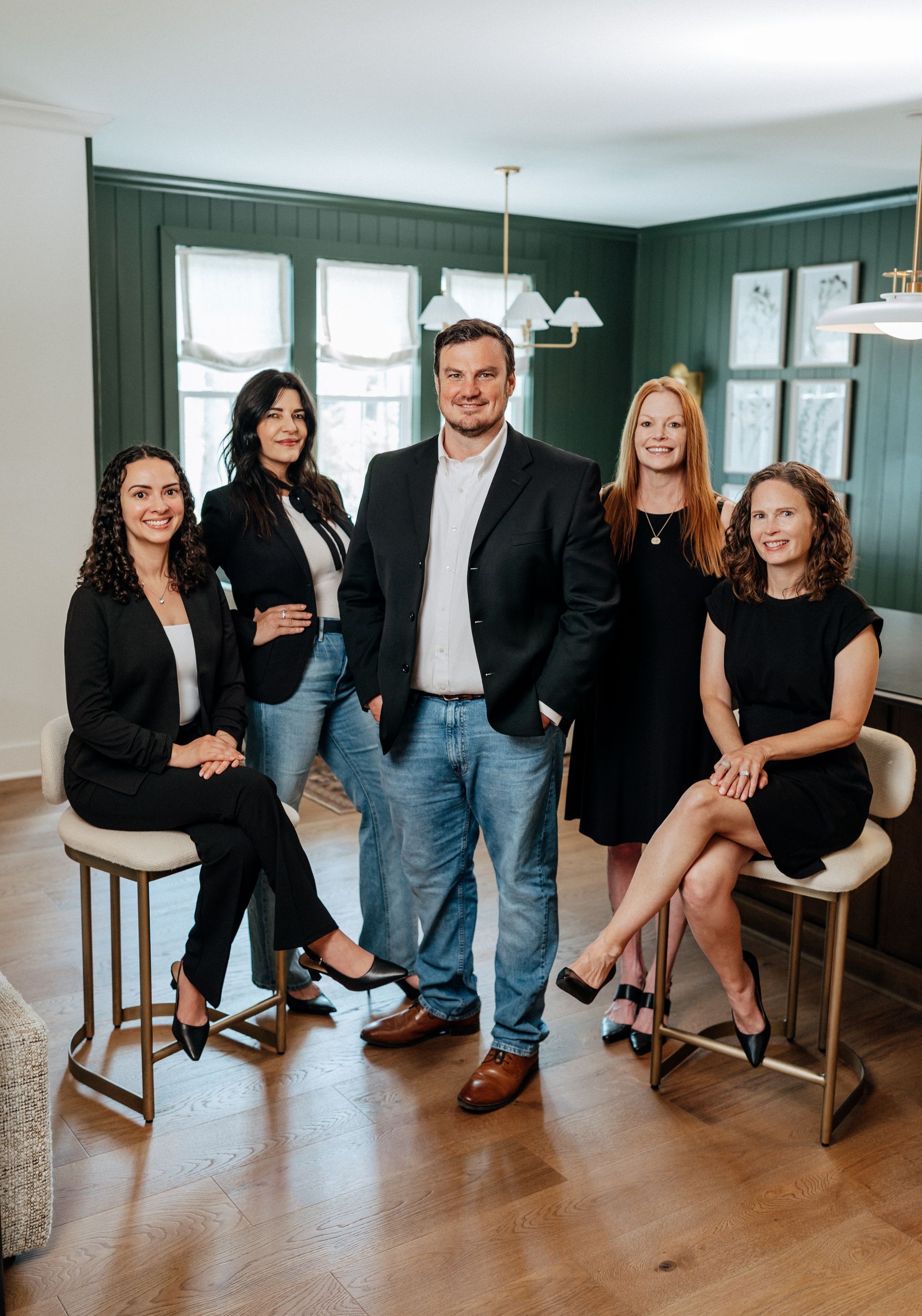 Five adults posing in a living room, with gray walls, large windows, and wood floors.