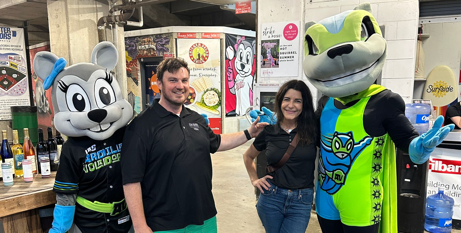 Two mascots and two people posing inside a shop, with one mascot holding a drink