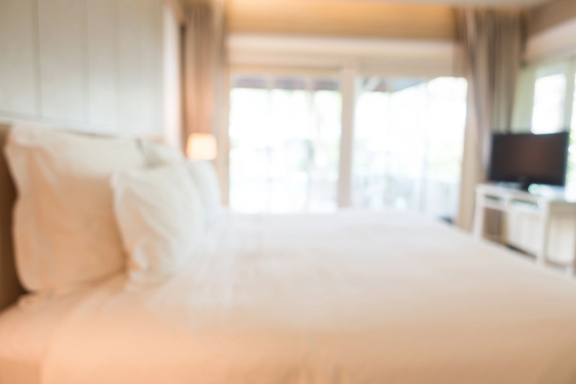 Camera da letto luminosa e con luce soffusa, dotata di un ampio letto, arredi bianchi e porte scorrevoli in vetro che conducono a un balcone.