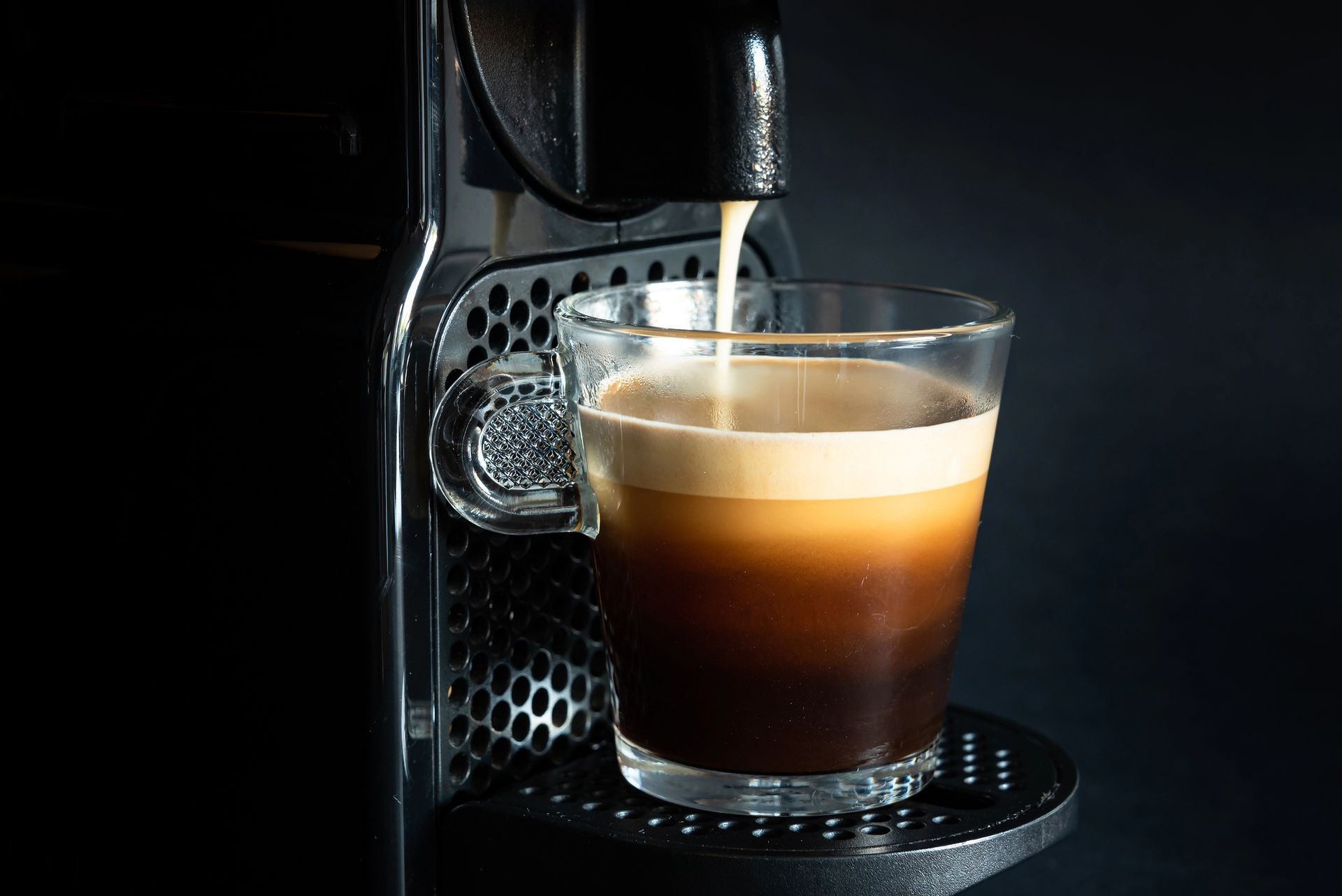 Un bicchiere di caffè a strati sotto una macchina da caffè che eroga espresso.