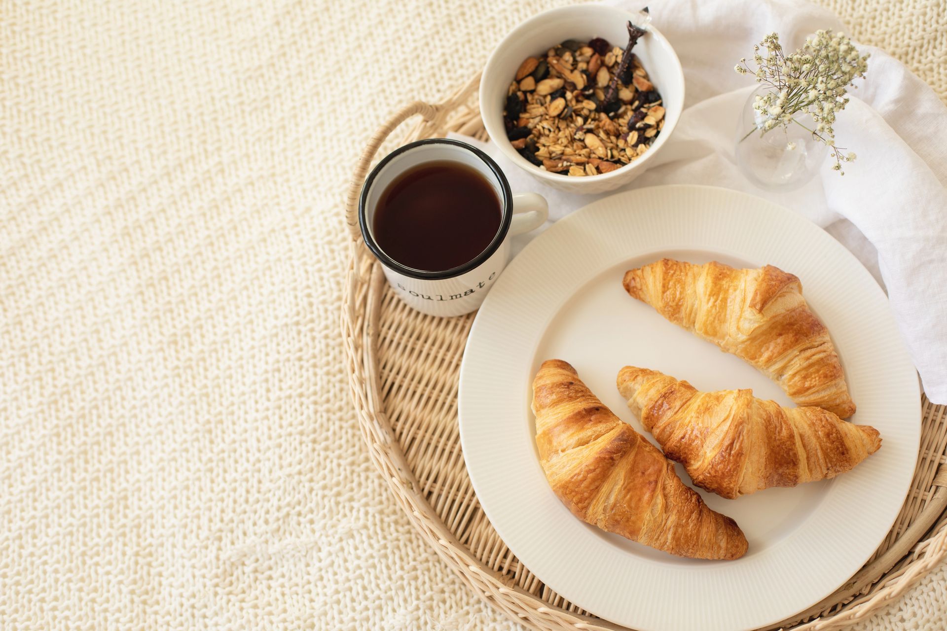 Cornetti su un piatto bianco con caffè e granola su un vassoio di vimini