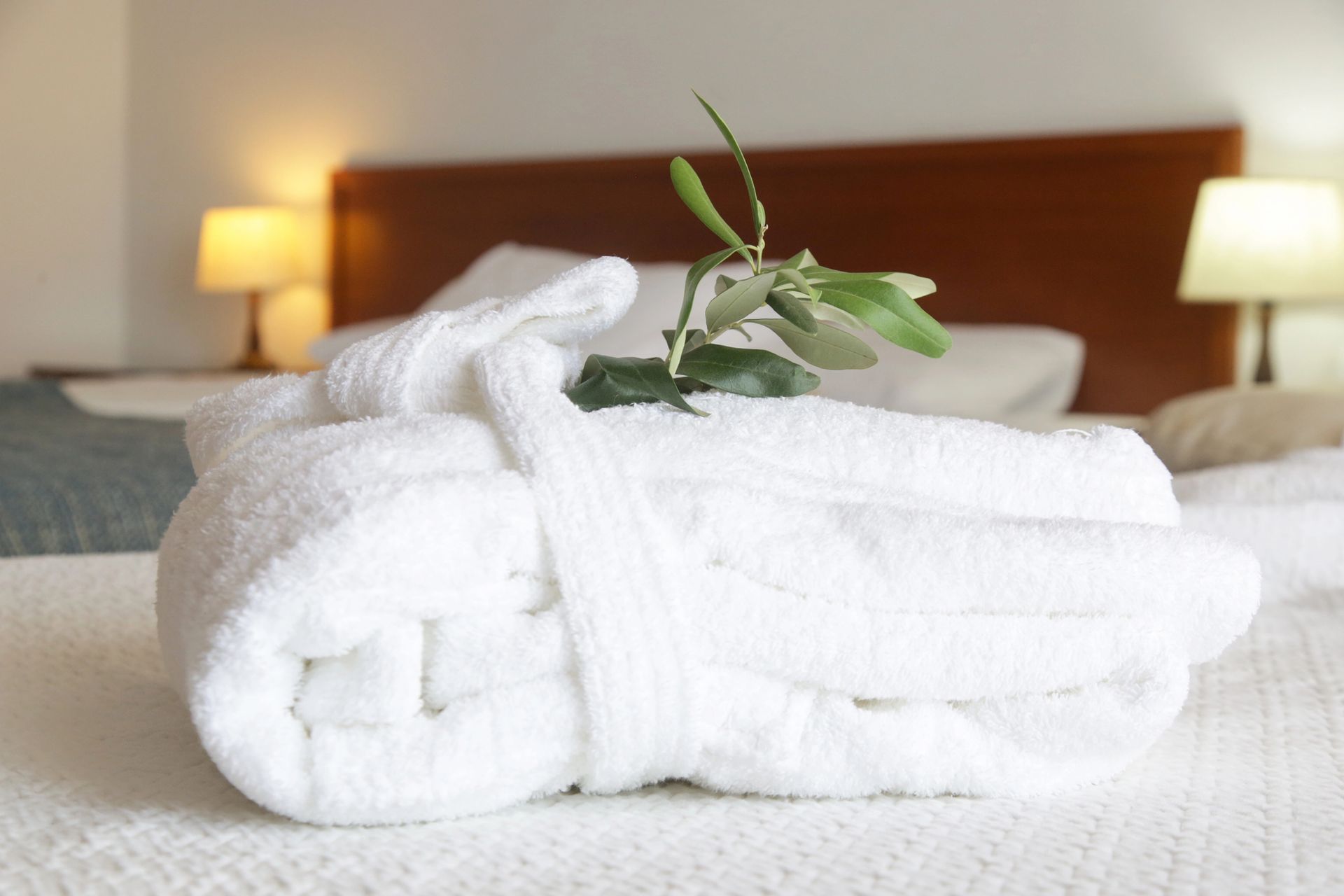 Asciugamani bianchi disposti su un letto in una camera d'albergo, con una piccola foglia verde sopra.