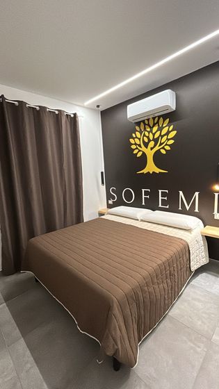 Camera da letto luminosa e con luce soffusa, dotata di un ampio letto, arredi bianchi e porte scorrevoli in vetro che conducono a un balcone.