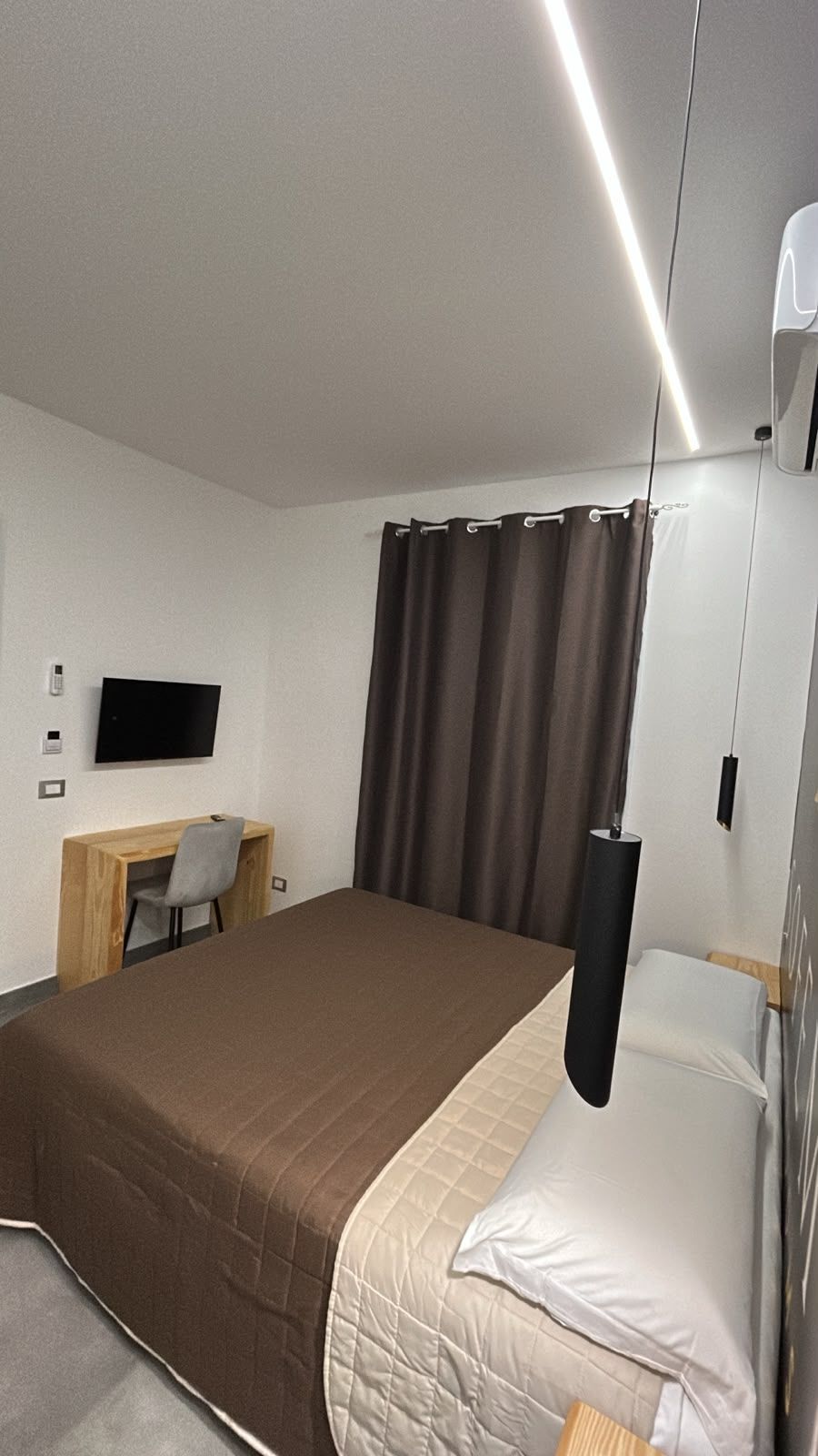 Asciugamani bianchi arrotolati su un letto ben rifatto con una coperta grigia e una lampada da comodino dalla luce soffusa.