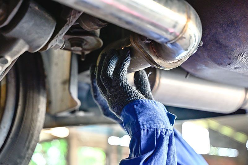 Gloved hands wiping a metal car exhaust pipe under a vehicle