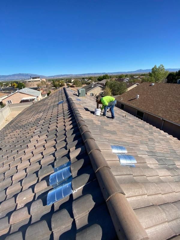 Person painting roof tiles on a residential roof under a clear blue sky.