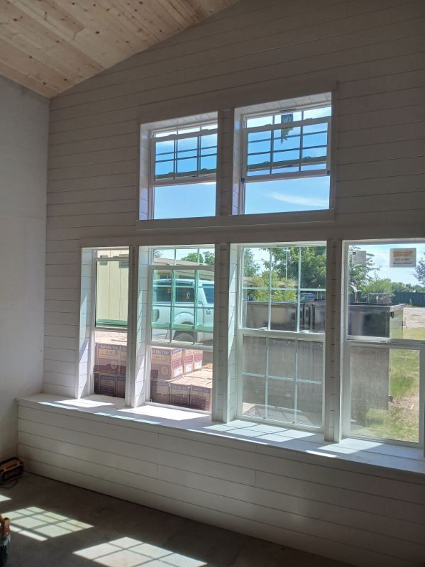 Interior with white-paneled walls, large windows, and a window seat; sunlight streams in.
