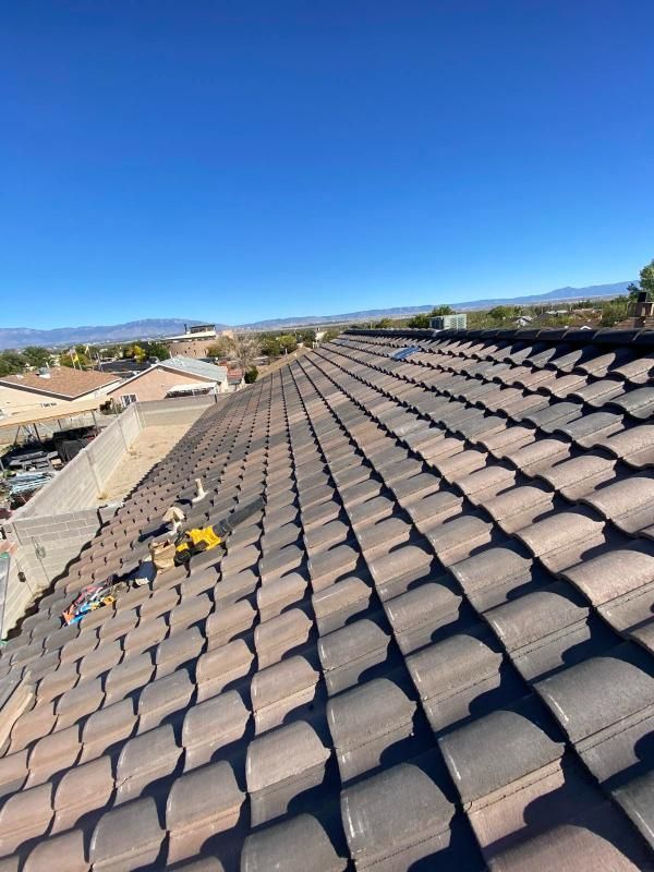 A brown tile roof under a clear blue sky, tools visible.