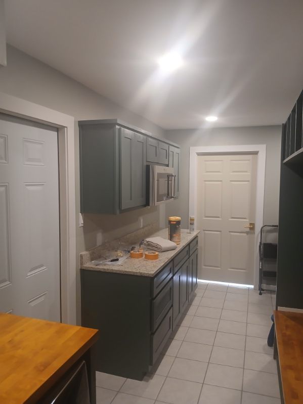 Kitchen with gray cabinets, countertop, and white tile floor. Two white doors and a wooden table are visible.